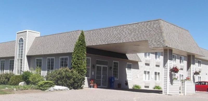 The Cedarville Hotel exterior — a long two-storey building with a grey shingled roof, a covered drive-through entrance portico and landscaped beds along the front.