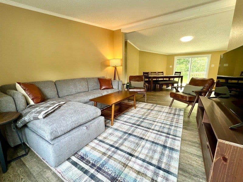 Open concept living area in the 3 Bedroom House, with a large sectional sofa, armchairs, a dining table seating six and sliding doors to the backyard