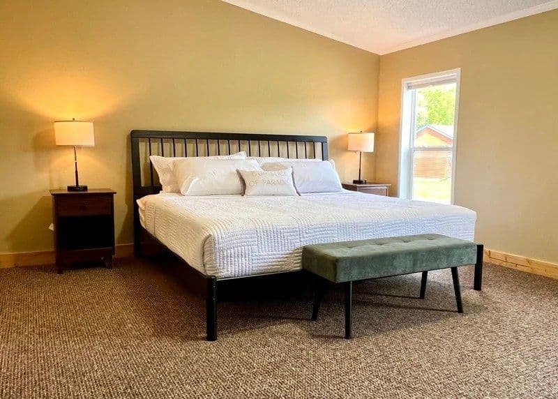 Master bedroom in the 3 Bedroom House, with a king bed, bedside lamps and an upholstered bench at the foot of the bed